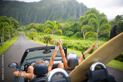 Road trip travel - girls driving car in freedom. Happy young girls cheering in convertible car on summer Hawaii vacations. photo