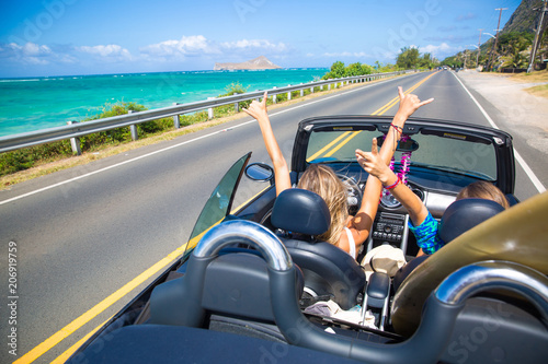 Road trip travel - girls driving car in freedom. Happy young girls cheering in convertible car on summer Hawaii vacations. photo