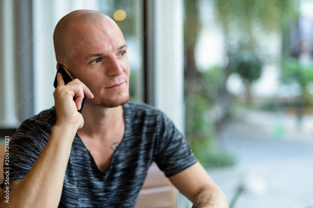 Young handsome bald man thinking while talking on mobile phone i Young handsome bald man thinking while talking on mobile phone i