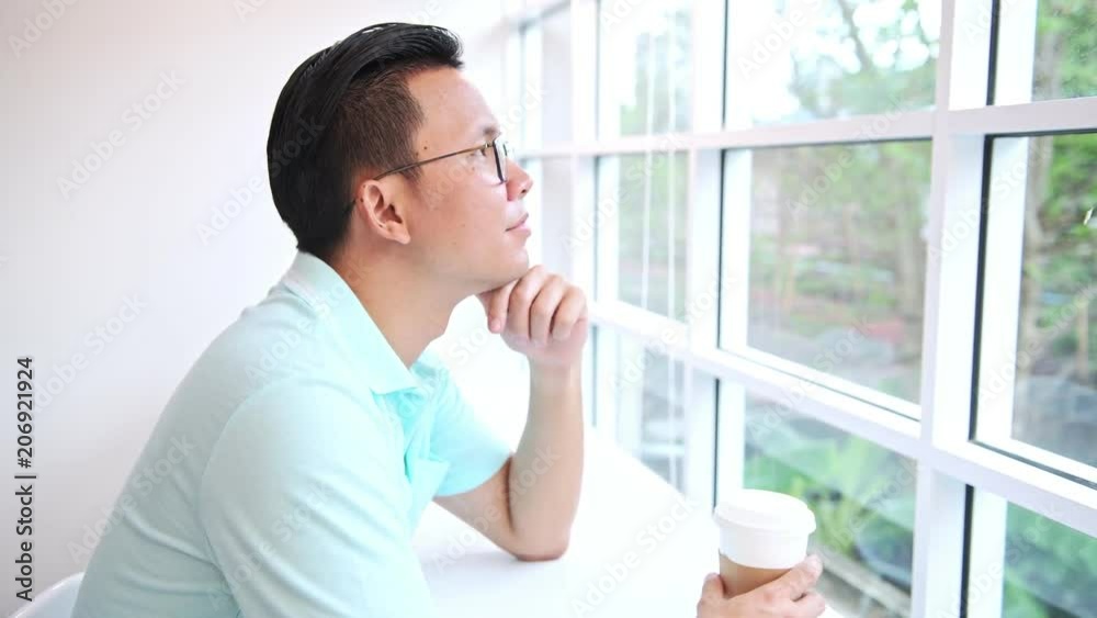 Casual business man working in coffeeshop. Young asian man sitting in coffee shop thinking and holding coffee cup.. Casual business man working in coffeeshop. Young asian man sitting in coffee shop thinking and holding coffee cup..