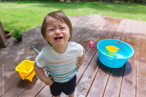 Upset crying toddler boy playing with water outside
