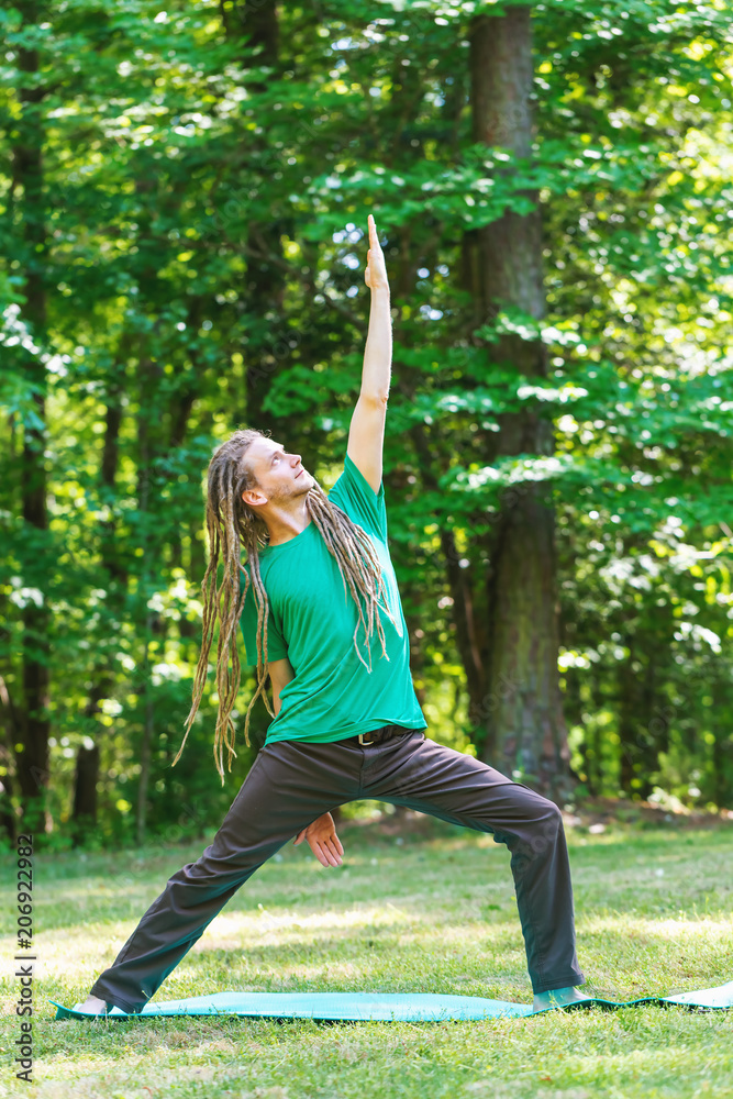 Man in a yoga pose outside in a field surrounded by forest