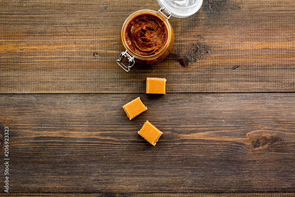 Caramel sauce in glass jar near caramel cubes on dark wooden background top view copy space Caramel sauce in glass jar near caramel cubes on dark wooden background top view copy space