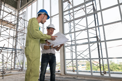 Asian male engineers wear helmet. he stand watching the building structure and blueprint in hand. concept check the quality inspection