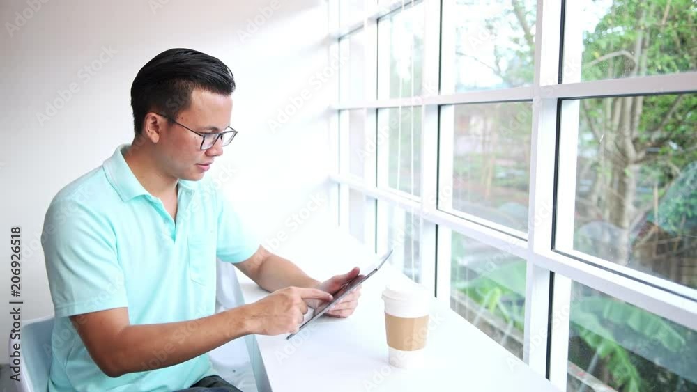 Casual business man working in coffeeshop. Young asian man sitting in coffee shop using his tablet. Casual business man working in coffeeshop. Young asian man sitting in coffee shop using his tablet.