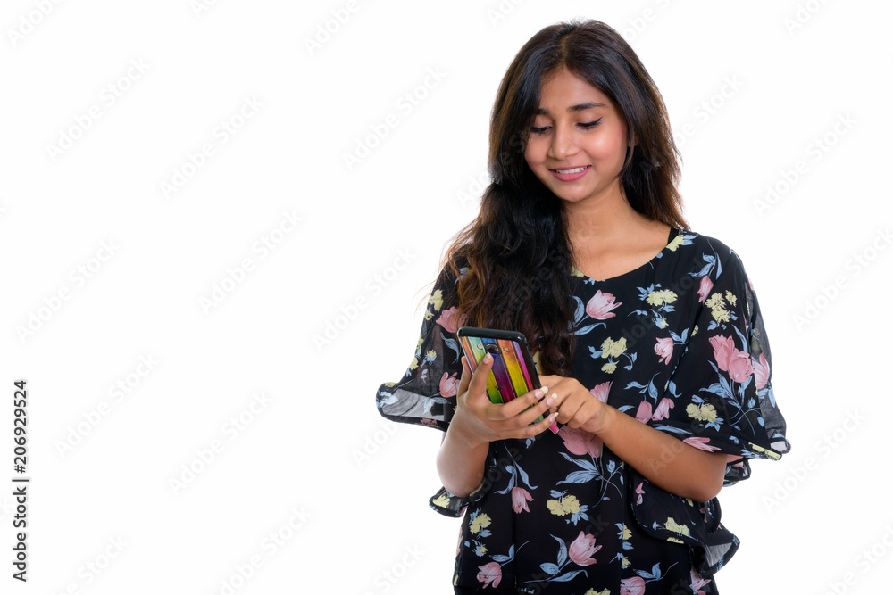 Studio shot of young happy Persian woman smiling while using mob Studio shot of young happy Persian woman smiling while using mob