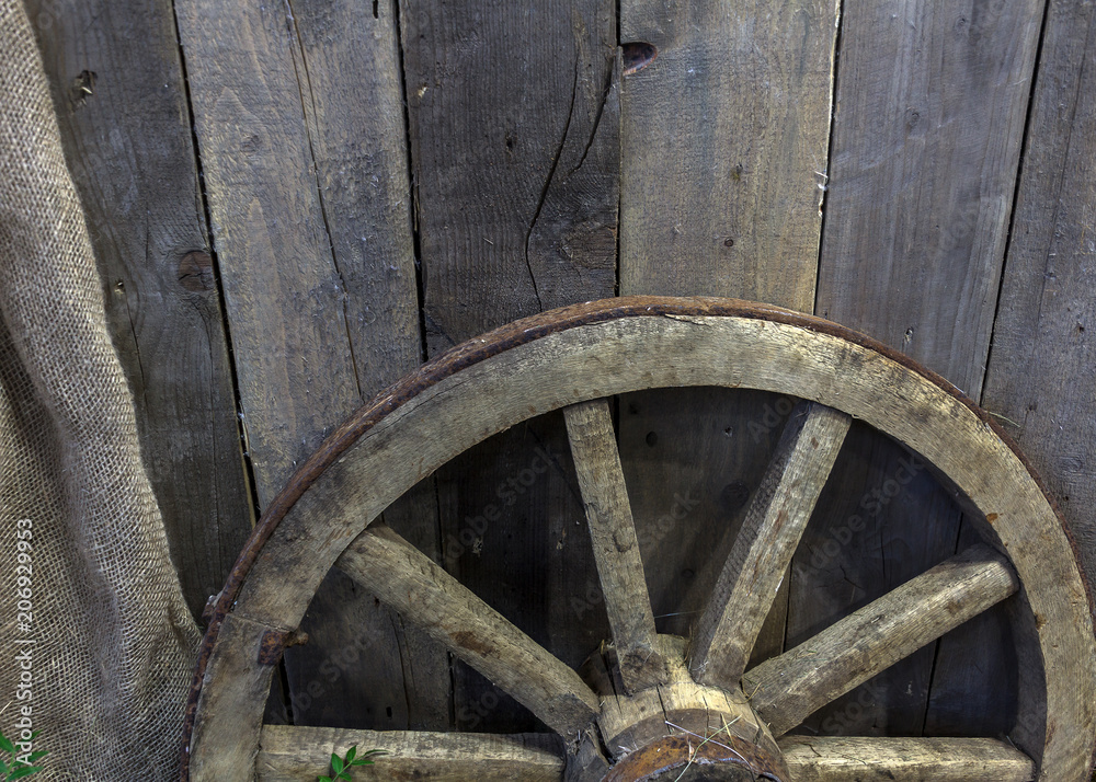 Wooden wheel of a cart leaning against a wooden wall