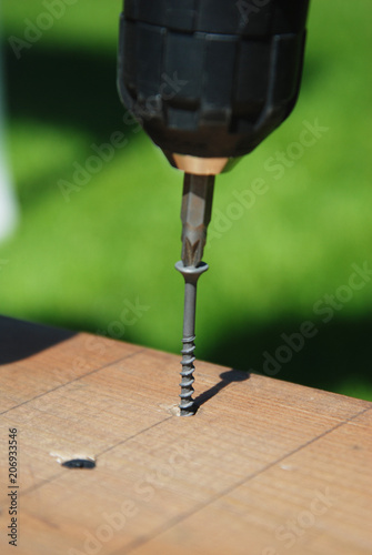Electric Screwdriver. Men working with a hand tool on the work bench Wooden Planks and Green grass Background. Outdoor Gardening.