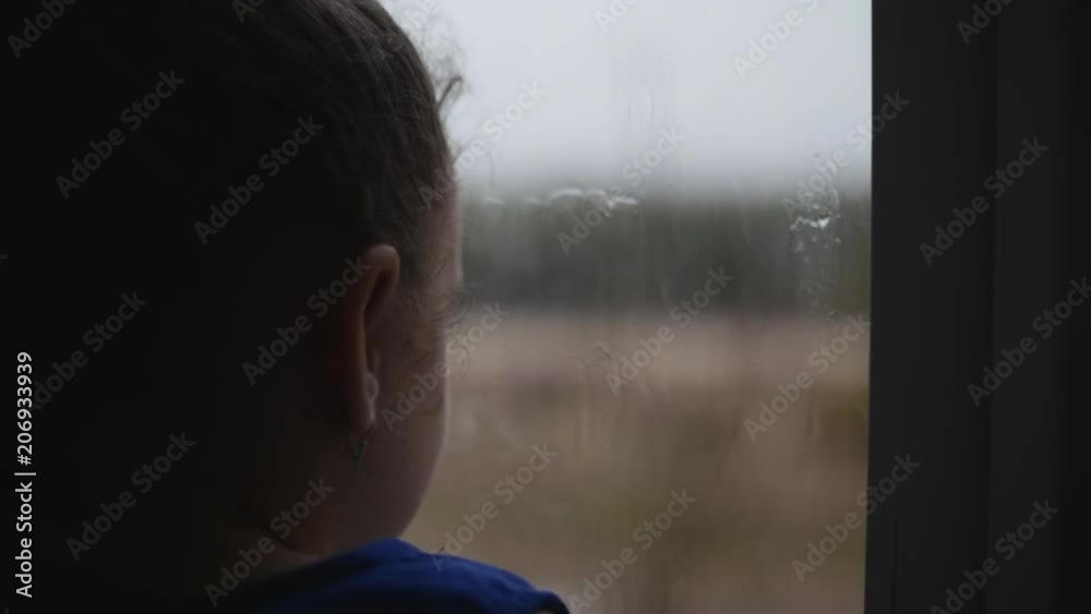 Child looks at the rain behind the window. Stock Footage.