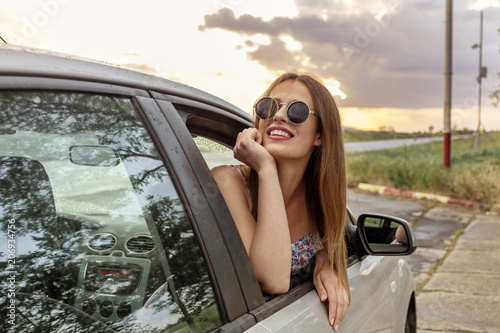 Young beautiful girl sitting on a car and looking thru the window and smile