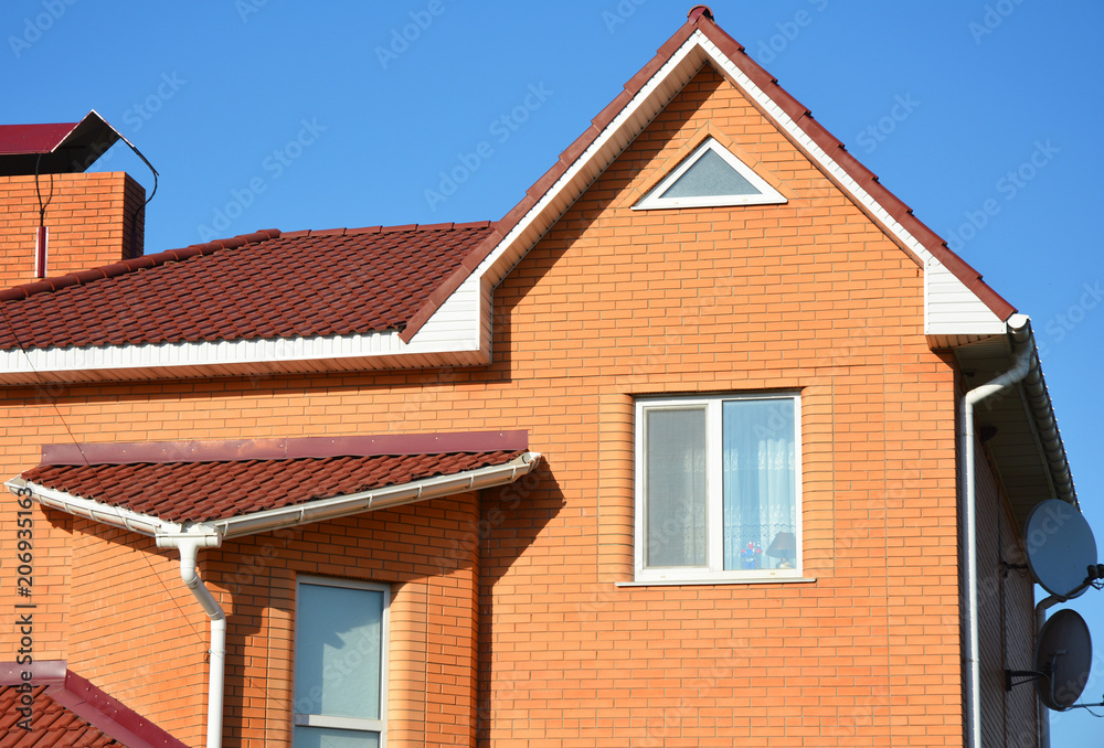 Close up on brick house with asphalt shingles roof and rain gutters in problem area.