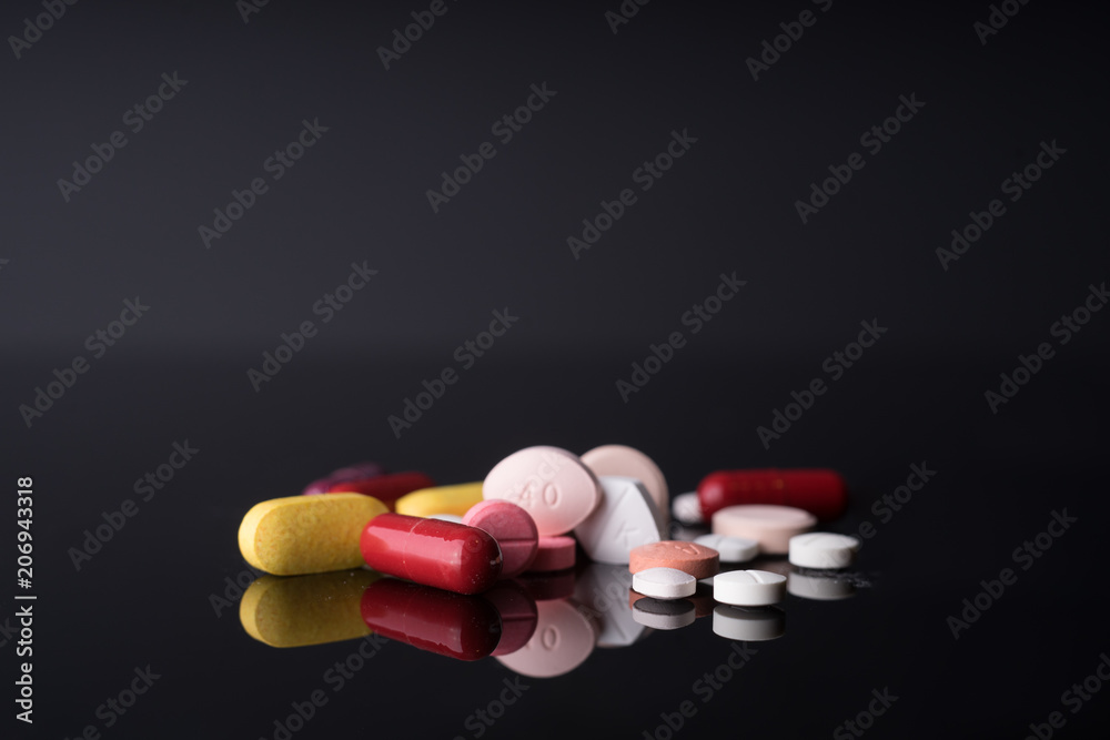 Medical pills and supplement capsule on black glass table with reflection.Studio shot.