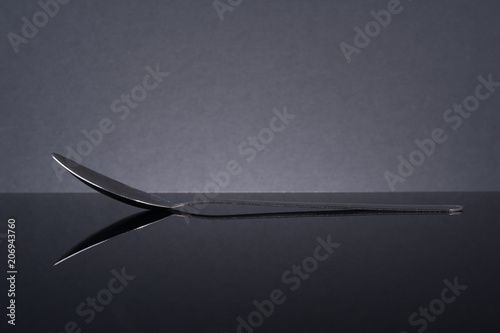 Steel spoon on black glass table with reflection.