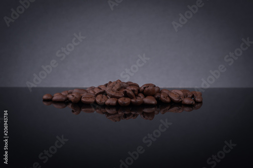 Roasted coffee beans spilled out from a cup and bottle on black glass table with reflection and smoke effect. © Apiq Sulaiman