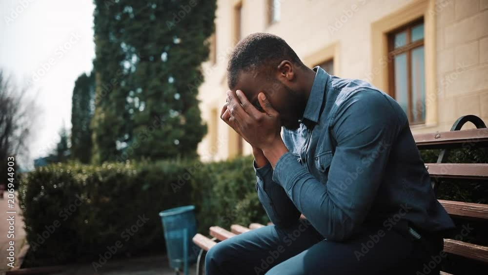 Sad and depressed young black african businessman sits tired after the call on the street. Concept of bad news, disappointment, illness