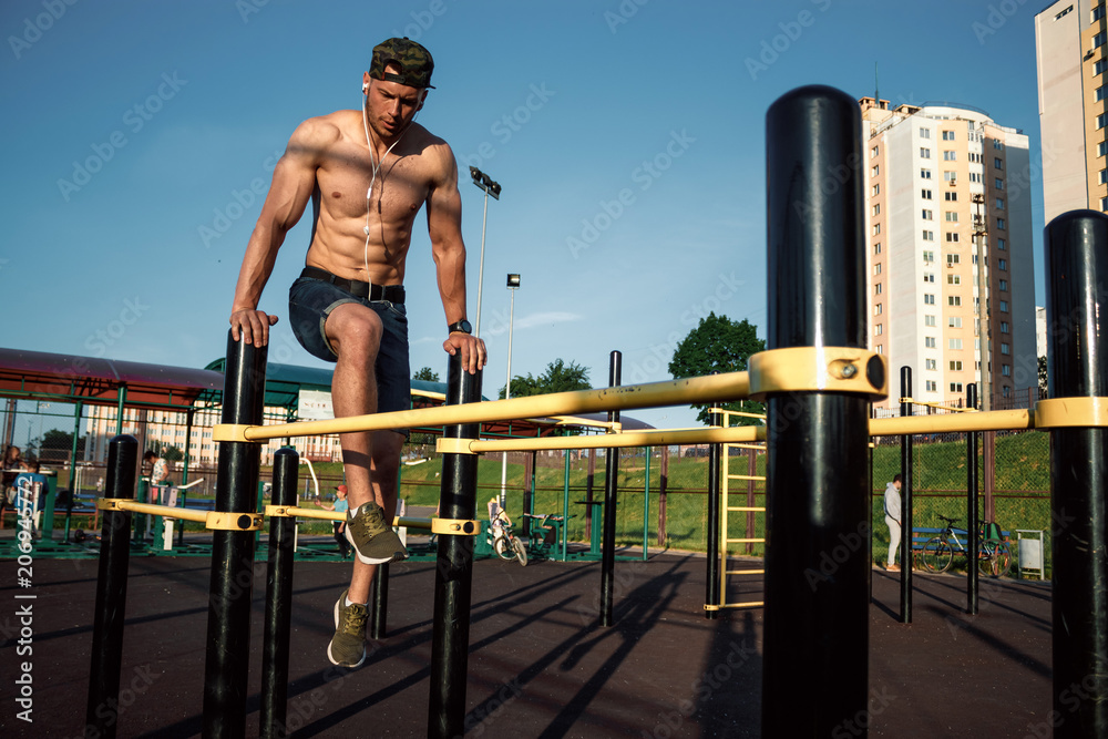 Young man doing exercises on the uneven bars in the stadium, athlete, outdoor training in the city copy space