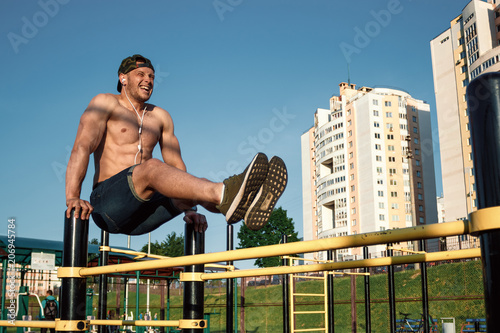 A young man raises his legs on a sports ground, an athlete, outdoor training in the city, a press exercise copy space