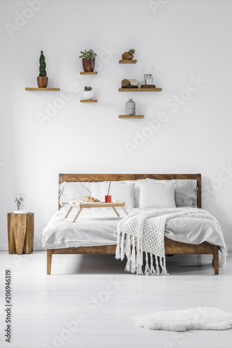 Front view of a wooden framed double bed with linen, pillows and blanket in a contemporary bedroom interior of a hotel. Food tray with breakfast standing on the bed. Real photo.
