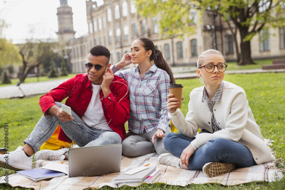 Tired student. Tired blonde-haired student in glasses feeling exhausted drinking coffee in the park