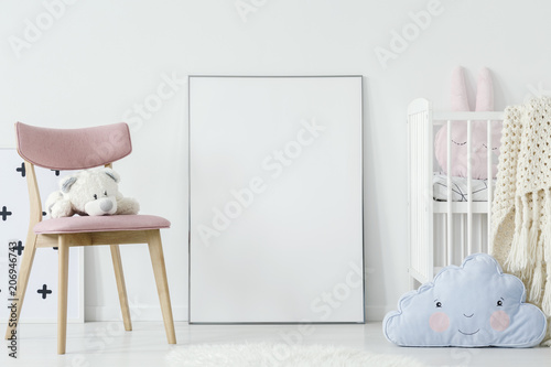 Plush toy on pink chair and blue pillow in child's room interior with mockup of poster. Real photo
