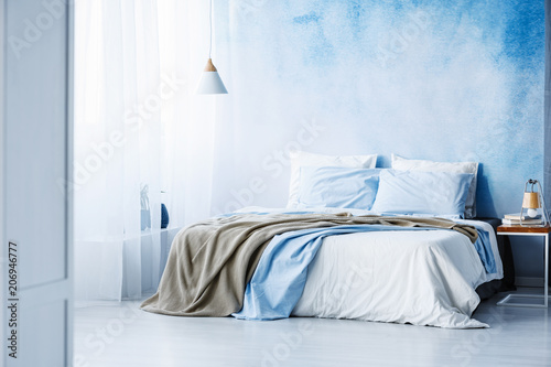Yellow and blue bedding on white bed in minimal bedroom interior with lamp on wooden table © Photographee.eu