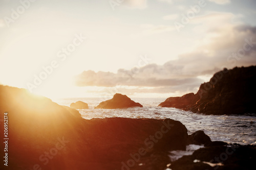 Sun shines over the sea waves and black rocks on the shore