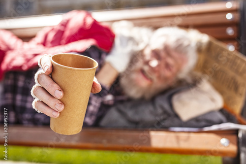 Money for living. Selective focus of a cup for money donations being held be a poor homeless man