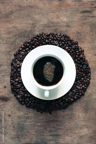 A mug of coffee on a wooden table surrounded by coffee beans