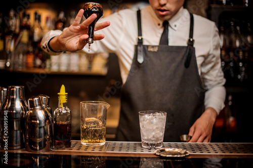 Brunet bartender adding an alcoholic essence into the mixing glass