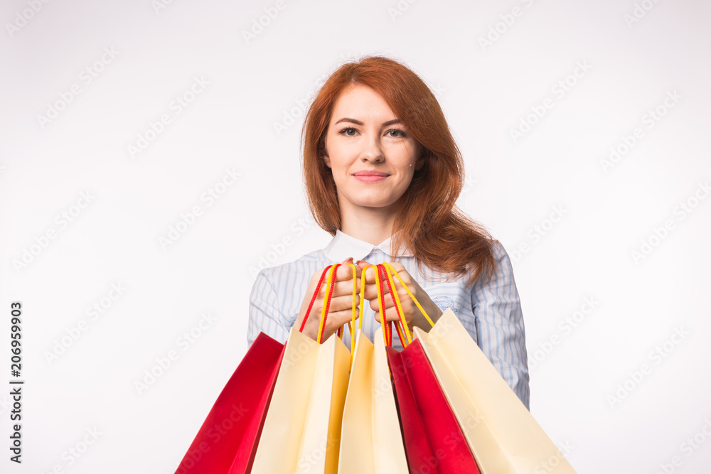 Portrait of young happy red-haired woman with shopping bags on white background