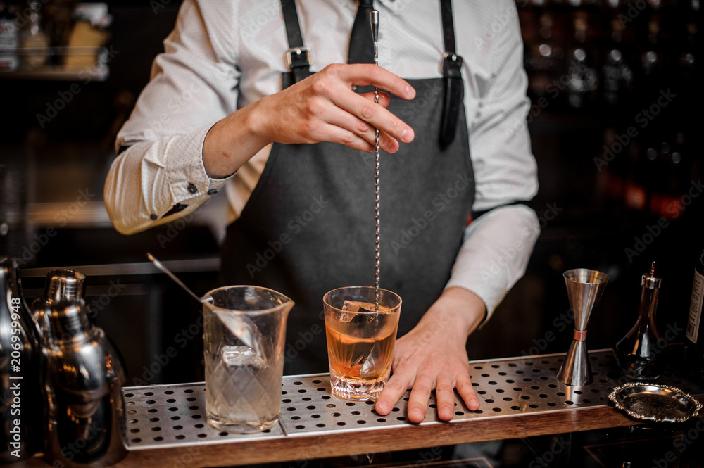 Bartender stirring a fresh cocktail in the ornate glass on the bar counter
