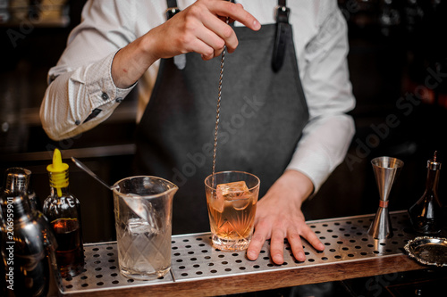 Bartender stirring cocktail in the ornate glass on the bar counter