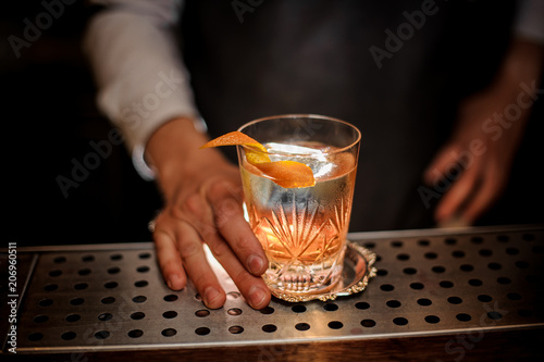 Bartender serving a summer fresh alcoholic cocktail with an orange zest
