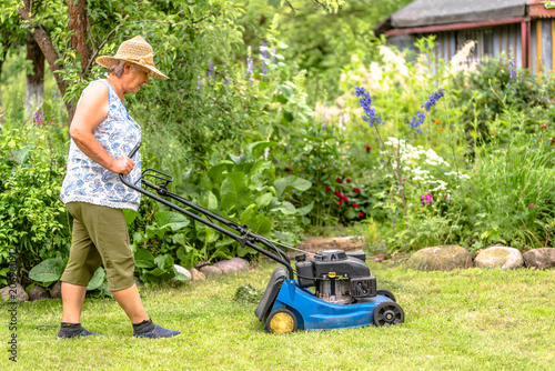 Woman gardener working in the garden, cutting grass with a mower, summer gardening
