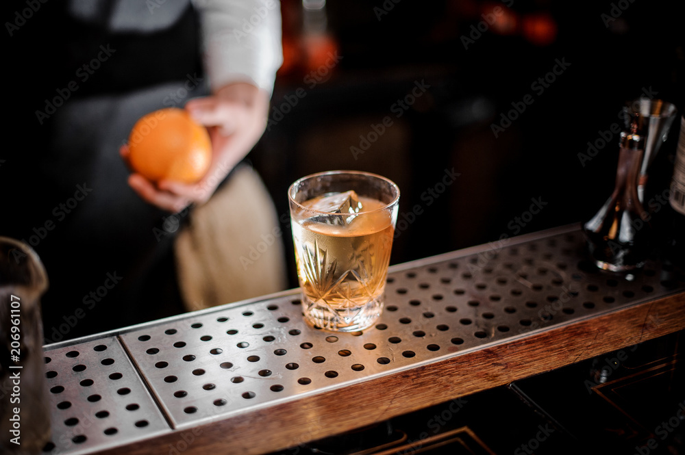Bartender holding the orange near the fresh alcoholic drink