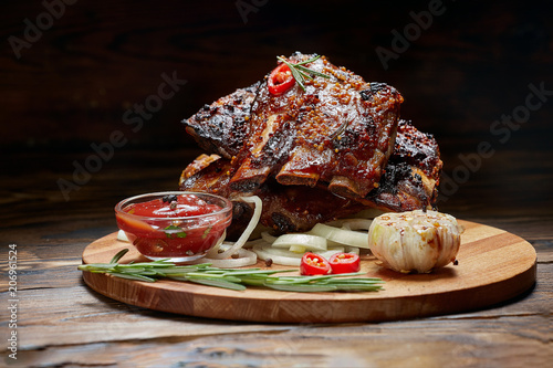 Fried ribs with rosemary, onion, sauce on a wooden round Board. Dark background. Place for text, copyspace