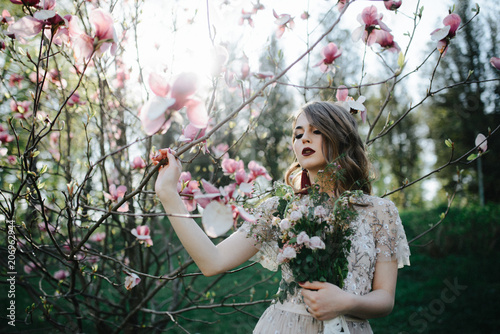 very beautiful girl the bride under a veil, beige wedding dress near the tree Sakura is looking down, nature photo