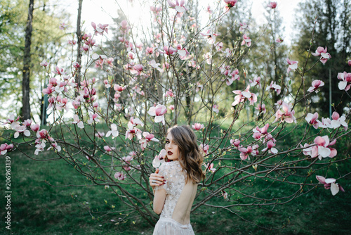 very beautiful girl the bride under a veil, beige wedding dress near the tree Sakura is looking down, nature photo