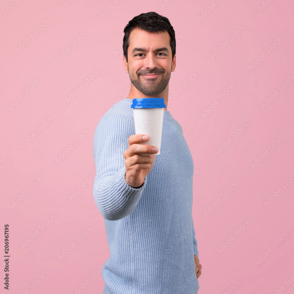 Man with blue sweater holding hot coffee in takeaway paper cup on pink background Man with blue sweater holding hot coffee in takeaway paper cup on pink background