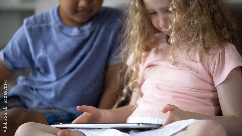Couple of little multiethnic children playing in educational app on tablet Couple of little multiethnic children playing in educational app on tablet