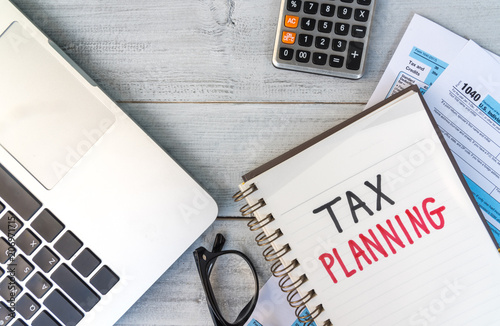 Tax planning hand written in a note with tablet, calculator, eyeglasses and tax return form on desk.