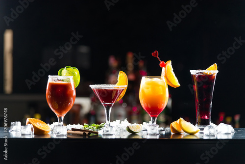 Multi-colored alcoholic cocktails with citrus in glasses of different shapes on the bar.