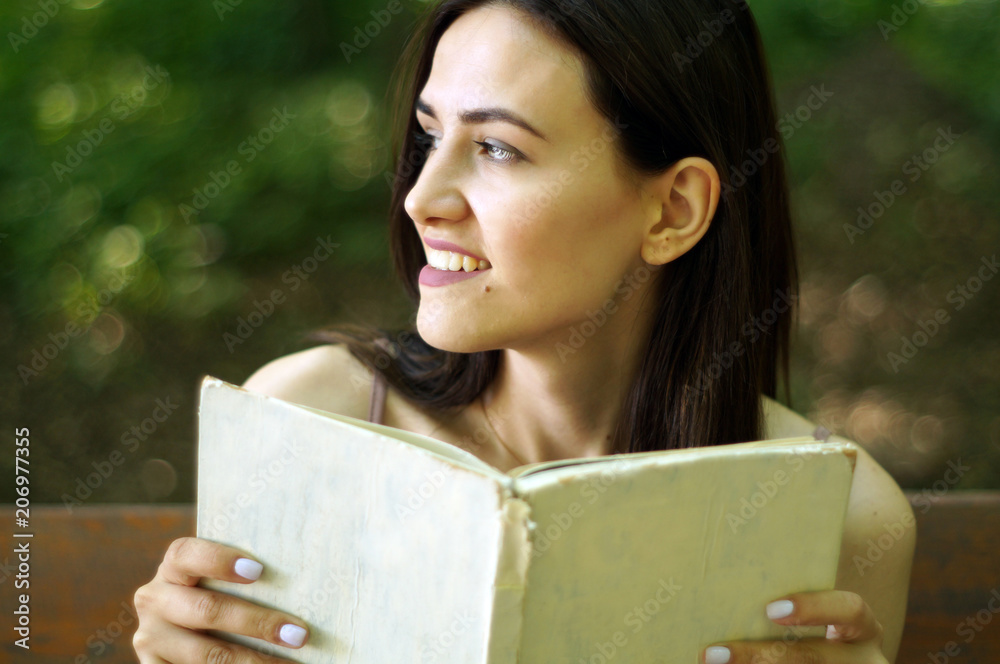 Pretty relaxed young beautiful woman reading a book on a bench with a shining sun. place for text Pretty relaxed young beautiful woman reading a book on a bench with a shining sun. place for text