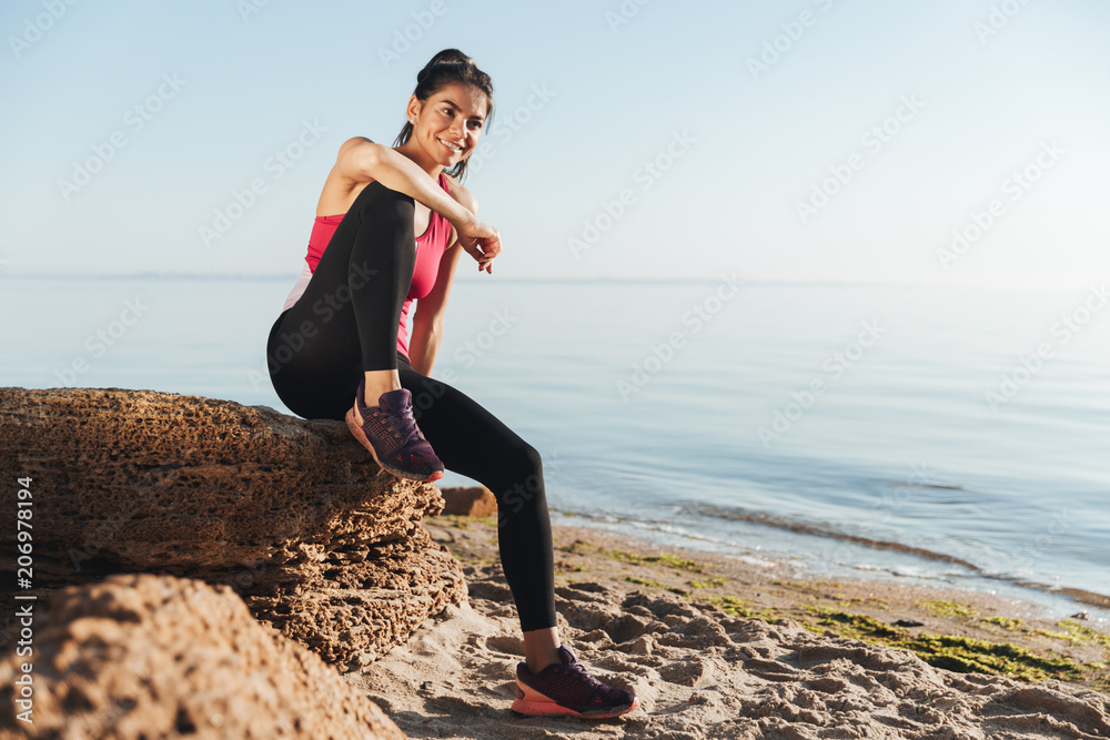 Smiling young sportswoman sitting on a rock