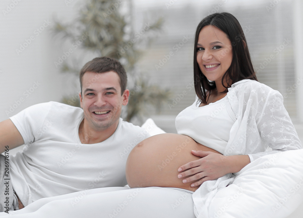 Laughing caucasian pregnant woman lying on bed with her husband in the bedroom Laughing caucasian pregnant woman lying on bed with her husband in the bedroom