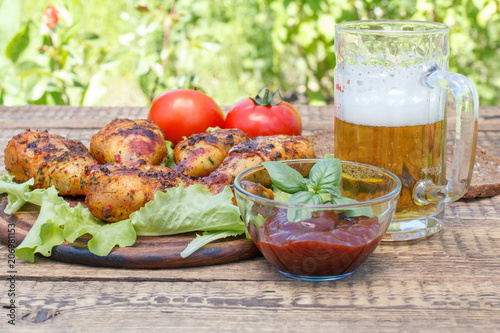 Grilled chicken legs and lettuce leaves on wooden chopping board  tomato sauce in glass bowl and glass mug of beer