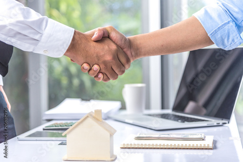 Concept of housing purchase and insurance, two business people estate agent with customer shaking hands after contract signature successful in real estate agency office