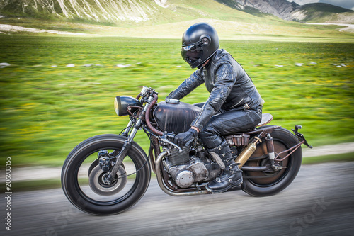Biker with black leather suit and mask riding on a custom special rat motorbike. Speed and freedom concept