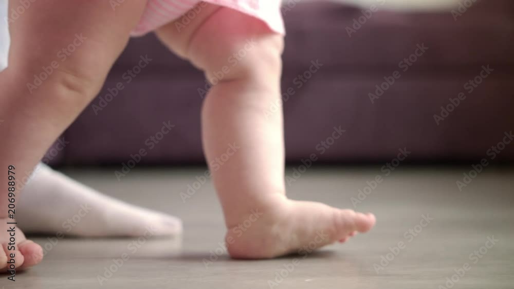 Baby learning walk. Close up of little feet doing first steps at home. Toddler walk on floor. Daddy support child in learning to go. Happy new life concept. Little feet step Baby learning walk. Close up of little feet doing first steps at home. Toddler walk on floor. Daddy support child in learning to go. Happy new life concept. Little feet step