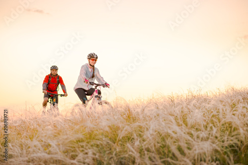 Young Couple Riding Mountain Bikes in the Beautiful Field of Feather Grass at Sunset. Adventure and Family Travel.